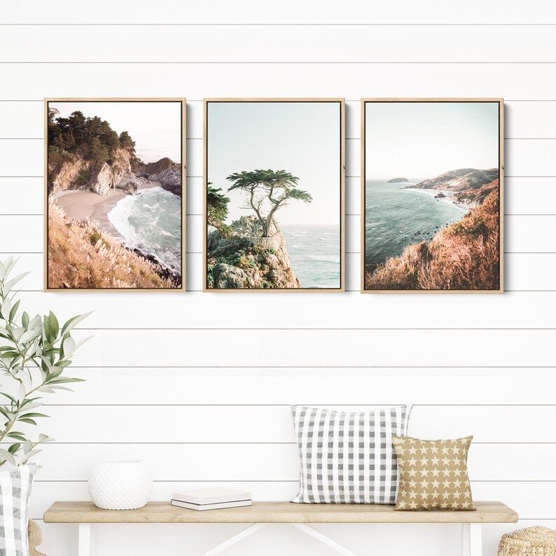 May include: Set of three framed landscape photographs featuring coastal scenes with a rocky coastline, ocean waves, and a lone tree on a cliff. The photos are in a rustic wooden frame.