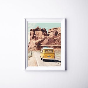 May include: A yellow vintage van drives down a road in a desert landscape with red rock formations in the background.