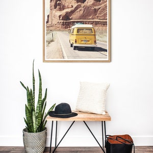 May include: A framed print of a yellow vintage van driving on a road through a desert landscape with red rock formations in the background.