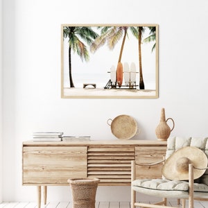 May include: A framed print of three surfboards leaning against a wooden stand, with palm trees in the background. The surfboards are white, orange, and blue.