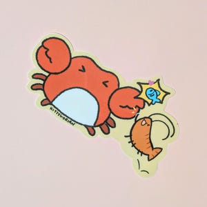 May include: A sticker featuring a cartoon crab with orange claws and body, a white belly, and brown legs. A small orange shrimp and a blue fish are also depicted. The sticker has the text "KITTYGORIAN" on it.