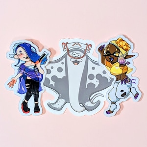 May include: Three colorful stickers featuring characters from a video game. One sticker depicts a blue-haired character holding a weapon, another shows a manta ray, and the third shows a character with brown skin and yellow clothing. The stickers are on a pink background.