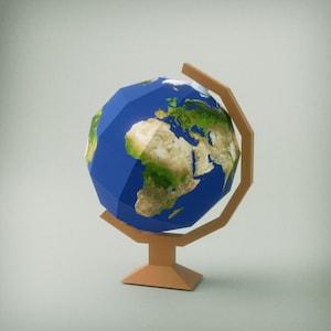 Puede incluir: Un globo terráqueo de estilo low-poly con océanos azules y continentes verdes y beige. El globo está montado sobre un soporte marrón claro. El soporte tiene una base y un marco curvo. El fondo es gris claro.