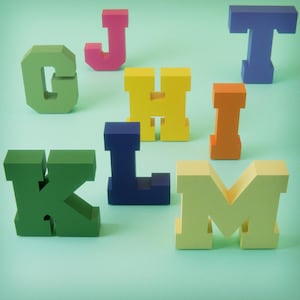 Puede incluir: Un conjunto de letras de madera geométricas y coloridas, incluyendo G, J, H, I, K, L, M y T, se disponen sobre un fondo verde claro. Las letras son de varios tonos de verde, rosa, amarillo, naranja, azul y amarillo claro.