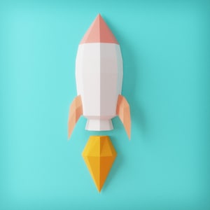Puede incluir: Un cohete de papel en blanco, melocotón y naranja, con una llama amarilla, sobre un fondo turquesa. El cohete tiene un diseño geométrico, con una parte superior puntiaguda y aletas anguladas. La llama tiene forma de diamante.