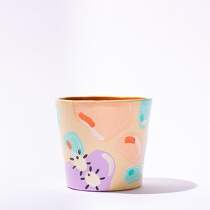 May include: A hand-painted ceramic planter with a light beige background and abstract shapes in shades of pink, purple, blue, and orange.