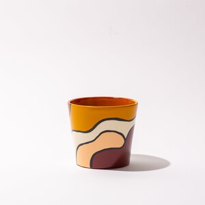 May include: A ceramic cup with a geometric pattern in shades of orange, yellow, white, and brown.