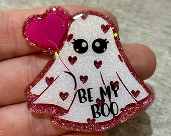 May include: A glittery white ghost-shaped charm with a pink heart balloon. The charm has red heart accents and a pink glitter border. Text on the charm reads "BE MY BOO".