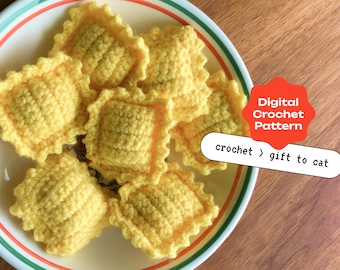 May include: A digital crochet pattern for a crocheted cat toy. The pattern is for a set of six yellow crocheted ravioli-shaped cat toys. The image shows the crocheted toys on a white plate with a green and red rim.