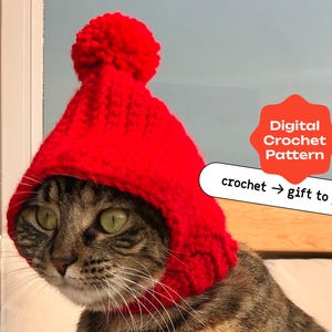 May include: A tabby cat wearing a red crocheted hat with a pom-pom on top. The hat has a hood that covers the cat's ears. The text "Digital Crochet Pattern" and "crochet -> gift to pet" is visible in the image.