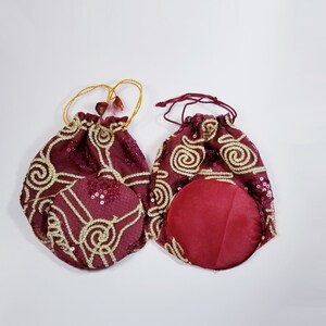 May include: Two burgundy drawstring bags with gold embroidery and sequins. One bag is open to show the burgundy lining.
