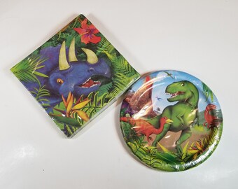 May include: A set of dinosaur-themed party supplies, including a paper plate and a paper napkin. The plate features a green Tyrannosaurus Rex dinosaur with a red and orange bird dinosaur and a smaller green dinosaur. The napkin features a blue Triceratops dinosaur with green foliage.