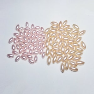 May include: A collection of oval-shaped pearl beads, some are a light pink color and others are a cream color.