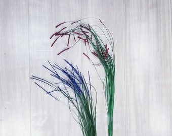 May include: Two bunches of artificial grass with decorative tips. One bunch has purple tips and the other has blue tips. The grass is green and the tips are sparkly.