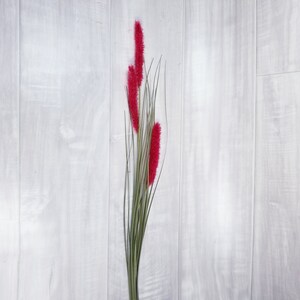 May include: A bunch of pink fluffy artificial flowers with green stems against a white wood background.