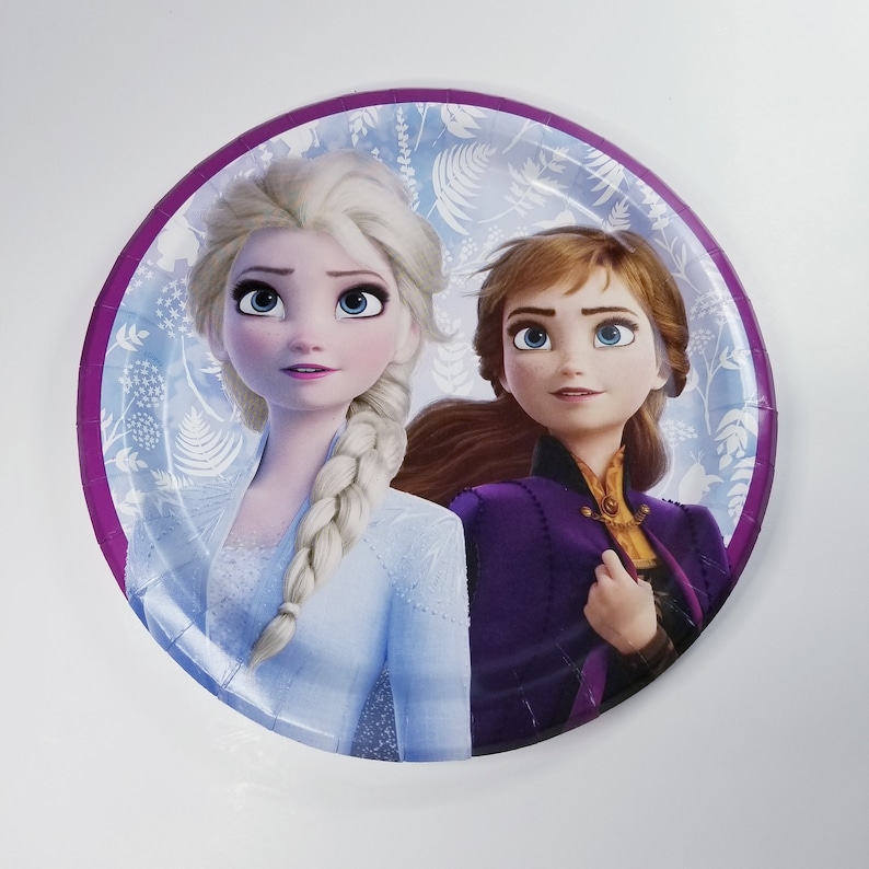 May include: A purple and white paper plate with a picture of Elsa and Anna from the movie Frozen. Elsa is wearing a light blue dress and Anna is wearing a purple dress.