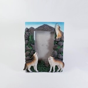 May include: A brown picture frame with a mountain scene and three wolves howling. The frame is made of resin and has a 4x6 inch opening.