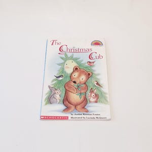 May include: A children's book titled "The Christmas Cub" featuring a cartoon bear holding holly. The cover art includes a Christmas tree, birds, and small animals. Published by Scholastic.