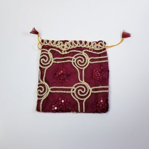 May include: A small burgundy drawstring bag with gold and red sequins. The bag has a geometric pattern with swirls and circles.