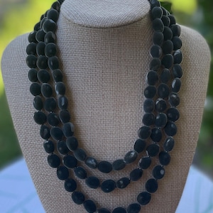 May include: A three-strand necklace with dark green oval beads. The necklace is displayed on a beige bust form. The beads have a slightly irregular shape and a matte finish, creating a classic and elegant look.