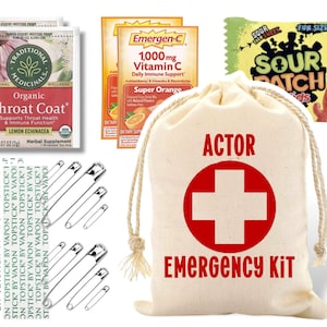 May include: A white canvas bag with the words "ACTOR EMERGENCY KIT" printed on it. The bag has a red cross symbol and a drawstring closure. The bag is surrounded by various items, including a box of throat lozenges, a box of vitamin C tablets, and a package of sour candy.