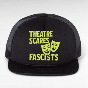 May include: Black trucker hat with a mesh back and a curved brim. The front of the hat features the text "THEATRE SCARES FASCISTS" in bright green, along with two theater masks.