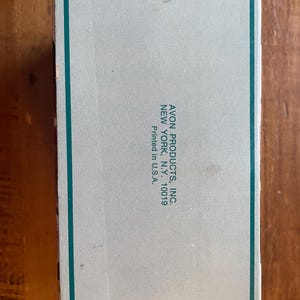 May include: A white cardboard box with green trim. The box has the text "AVON PRODUCTS, INC. NEW YORK, N.Y. 10019 Printed in U.S.A." printed on the side.