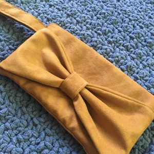 May include: A mustard yellow suede clutch with a large bow on the front.