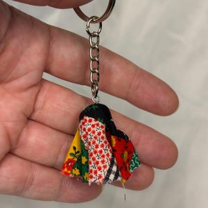 May include: A handmade keychain with a cluster of fabric scraps in red, yellow, green, and black floral patterns. The keychain has a silver metal ring and chain.