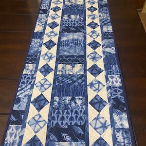 Könnte beinhalten: Ein blauer und weißer Tischläufer mit einem Rautenmuster. Der Läufer ist aus Stoff mit einem Batik-Muster.