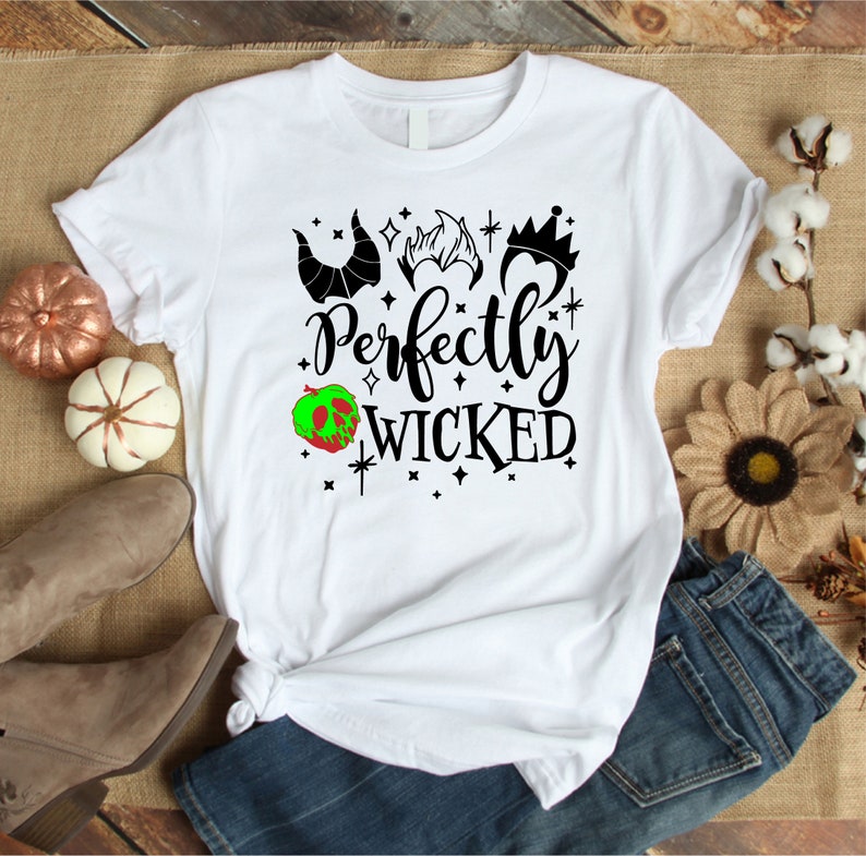K&ouml;nnte beinhalten: Wei&szlig;es T-Shirt mit einem schwarzen grafischen Design, auf dem "Perfectly Wicked" mit einem gr&uuml;nen Apfel und schwarzen Silhouetten von Kronen und H&ouml;rnern steht.