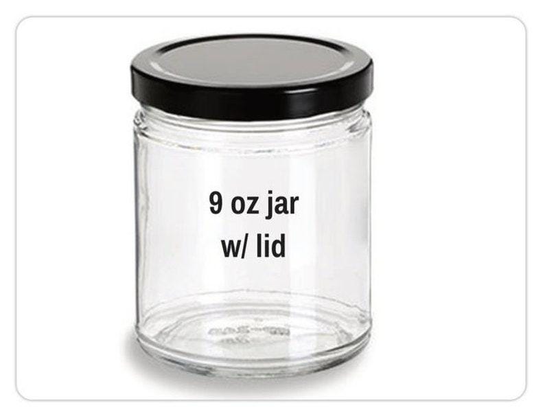 May include: A clear glass jar with a black lid. The jar is labeled "9 oz jar w/ lid". The jar is cylindrical and appears to be empty. The lid is a solid black color.