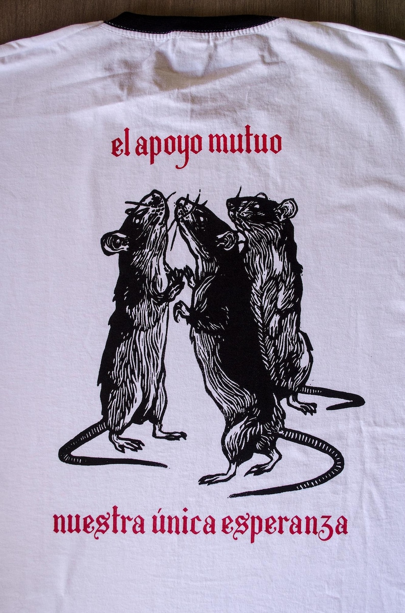 May include: White t-shirt with a black and white illustration of three rats standing on their hind legs. The text "el apoyo mutuo" is printed in red above the rats and "nuestra &uacute;nica esperanza" is printed in red below the rats.