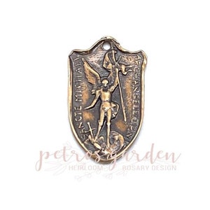 May include: A bronze-colored metal pendant featuring an image of Saint Michael the Archangel. The pendant is shaped like a shield and has the words "SANCTE MICHAEL" and "ORA PRO NOBIS" inscribed around the edge.