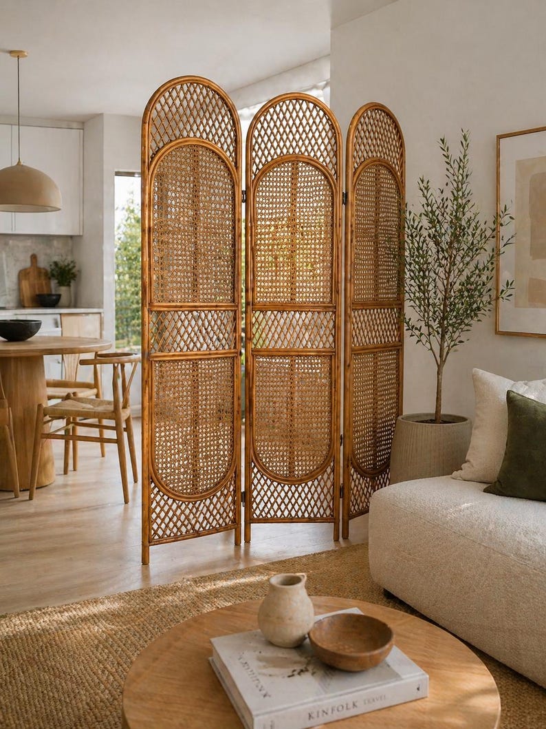 May include: A three-panel room divider made of woven rattan. The arched top and geometric patterns add a decorative touch. The natural brown color complements the neutral-toned living space. This screen is a stylish way to divide a room.