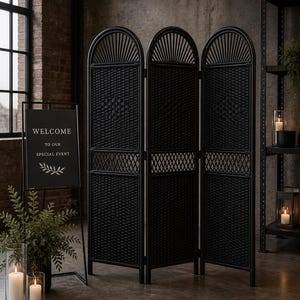 Puede incluir: Un biombo negro tejido con tres paneles, con la parte superior arqueada y un dise&ntilde;o de celos&iacute;a decorativa. Un letrero de bienvenida con el texto "WELCOME TO OUR SPECIAL EVENT" es visible. La escena incluye velas y vegetaci&oacute;n.