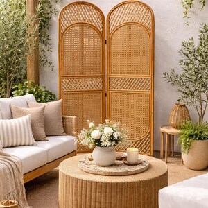 May include: A cozy outdoor living space featuring a woven rattan coffee table, a matching room divider, and a light-colored sofa with decorative pillows. A vase of white flowers and a candle sit on the table, creating a relaxing atmosphere.