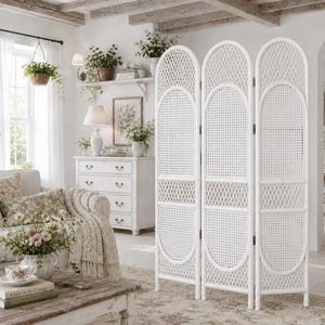 May include: A white, three-panel room divider with a woven rattan design. The divider has an arched top and oval accents. The room is decorated in a cottage style, with a white sofa, floral pillows, and a wooden coffee table.