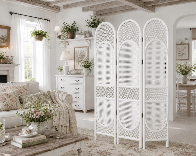 May include: A white, three-panel room divider with a woven rattan design. The divider has an arched top and oval accents. The room is decorated in a cottage style, with a white sofa, floral pillows, and a wooden coffee table.