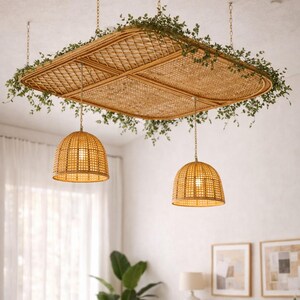 May include: A natural rattan ceiling light fixture with a square design, adorned with greenery. Two matching pendant lights hang below. The lampshades are made of woven rattan. The room has a neutral color palette.