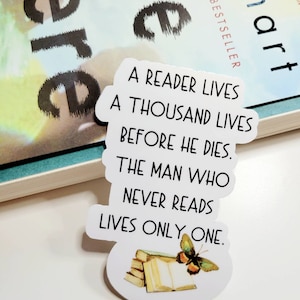 May include: White sticker with the quote "A reader lives a thousand lives before he dies. The man who never reads lives only one." The sticker has an illustration of books and a butterfly. A book is in the background.