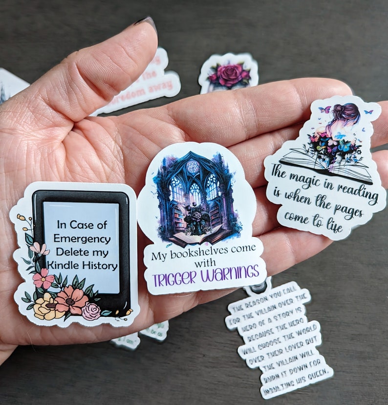 May include: Four book-themed stickers with colorful designs and text. The stickers feature a Kindle e-reader, a bookshelf with a gothic window, a book with flowers and a butterfly, and a book with the text "The magic in reading is when the pages come to life."