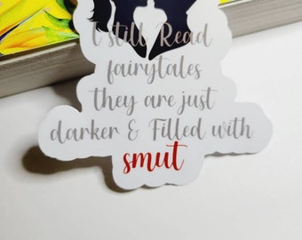 May include: A white sticker with a heart-shaped silhouette of a couple. The text reads "I still read fairytales they are just darker & filled with smut" in gray text with the word "smut" in red.