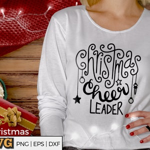 Könnte beinhalten: Weißes Langarmshirt mit schwarzem Text, der "Christmas Cheer Leader" lautet. Der Text ist in einer dekorativen, handschriftlichen Schriftart.