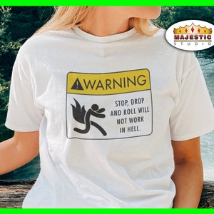 May include: White t-shirt with a yellow warning sign that says "WARNING! STOP, DROP AND ROLL WILL NOT WORK IN HELL."