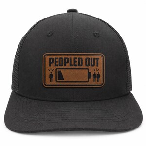 Può includere: Un cappellino da baseball nero con retro in rete e una toppa rettangolare marrone sul davanti. La toppa presenta la scritta "PEOPLED OUT" in nero, insieme a un'icona grafica di batteria scarica e due figure umane stilizzate ai lati.