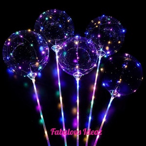 Puede incluir: Cinco globos de plástico transparente con luces LED de colores en su interior. Los globos están unidos a palos con luces LED que cambian de color. Los globos están sobre un fondo negro.