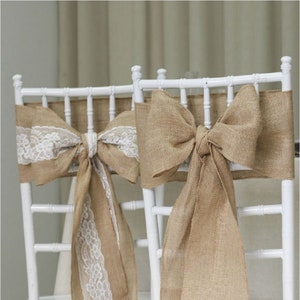 May include: Two white chairs with burlap sashes tied in bows. One chair has a white lace trim on the sash.