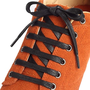 May include: Close-up of orange suede shoes with black shoelaces tied in a criss-cross pattern.