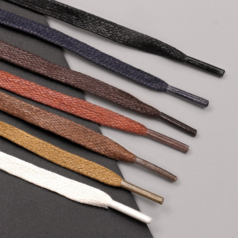 May include: A set of eight shoelaces in various colours, including black, navy blue, brown, red, and white. The shoelaces are arranged in a fan shape, with the darkest colour at the top and the lightest colour at the bottom.